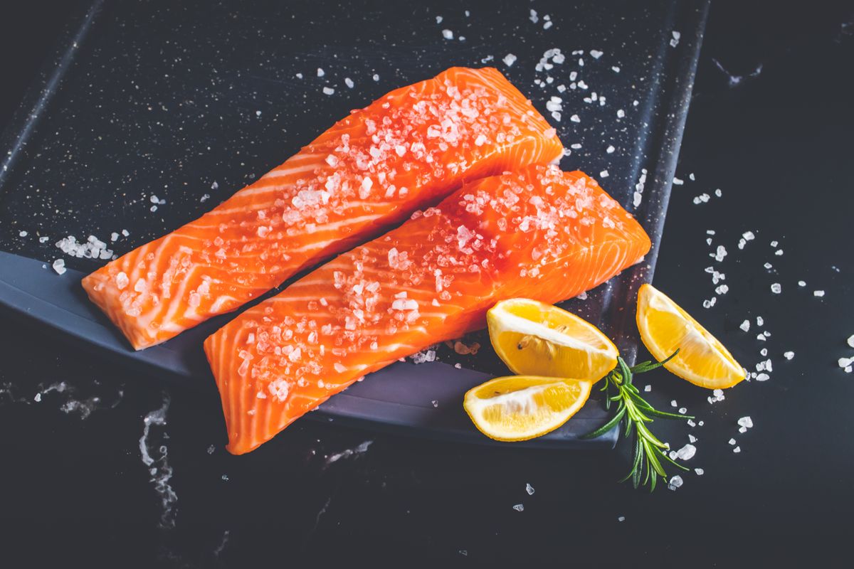 Raw salmon fillets with salt and lemon wedges on a tray